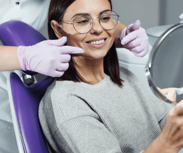 Woman sitting in a dental chair holding a mirror smiling. 