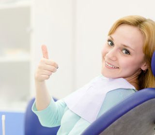 A woman sitting in a dental chair with a thumbs up